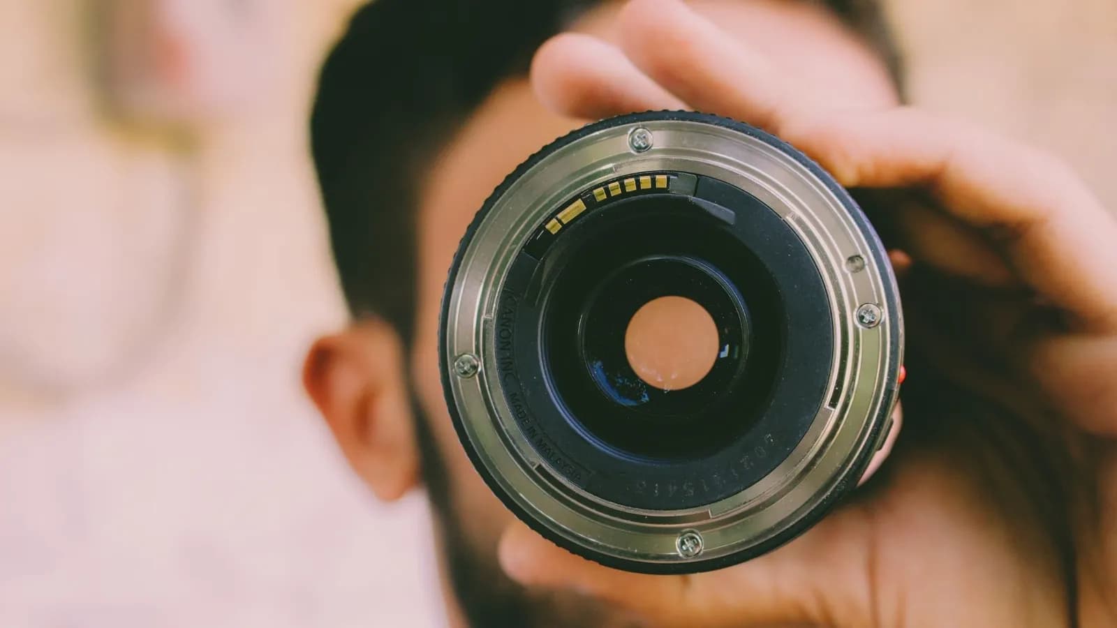 Gros plan de l'élément frontal d'un objectif Canon tenu devant le visage du photographe.