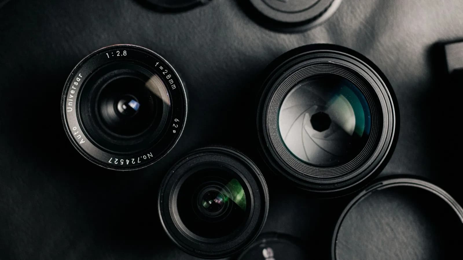 Plusieurs objectifs photo disposés à plat sur fond sombre, dont un objectif vintage 28 mm f/2,8.