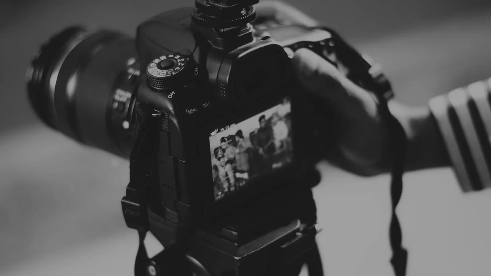 Dos d'un reflex sur trépied, molette des modes visible avec les positions M, Av, Tv et P, écran arrière affichant la scène cadrée, photo en noir et blanc.
